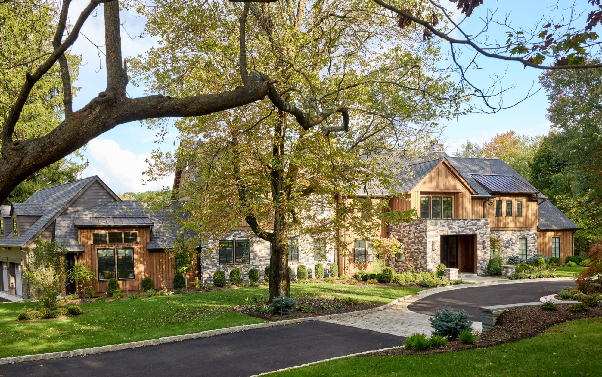 The same Mendham, New Jersey home after renovation, reclad in vertical cedar and stone with black windows, a new entry and a curved drive.
