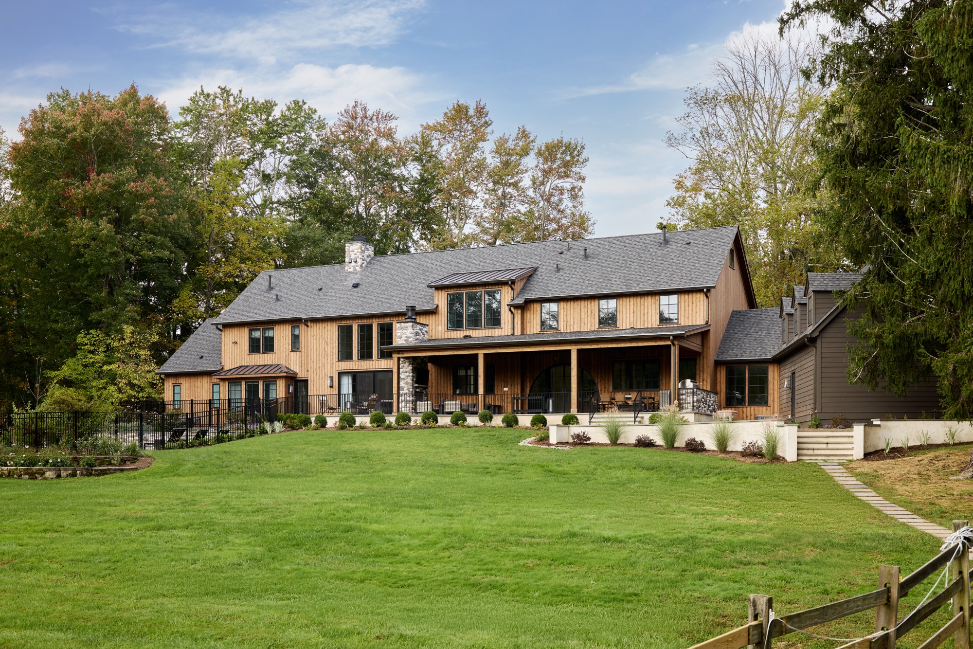 The renovated rear elevation in Mendham, New Jersey, in cedar and dark siding with a long covered porch, black windows and a terraced lawn.