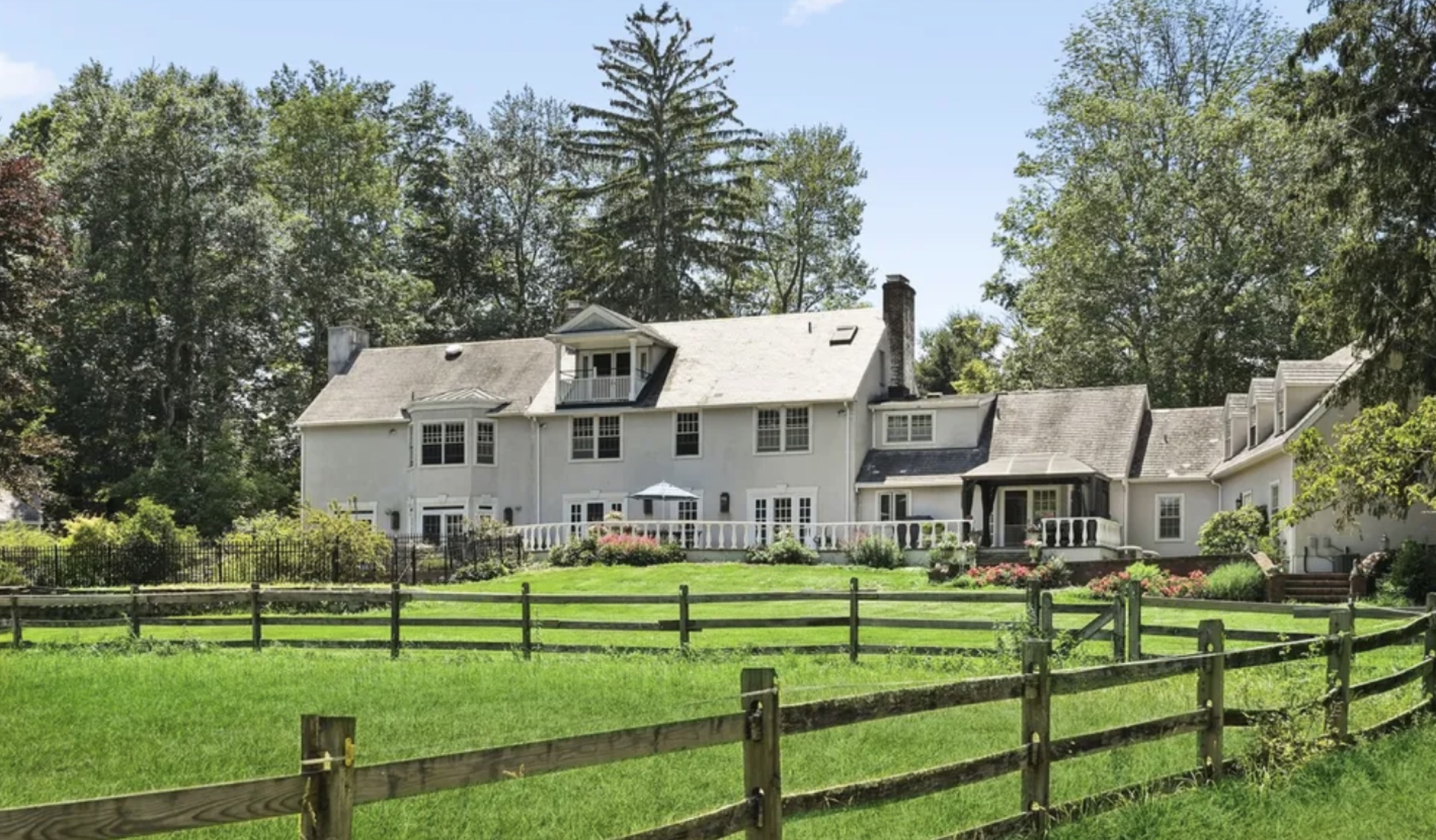Rear of the Mendham, New Jersey home before renovation — a white stucco rear elevation with a sunroom addition and a split-rail fence across the lawn.